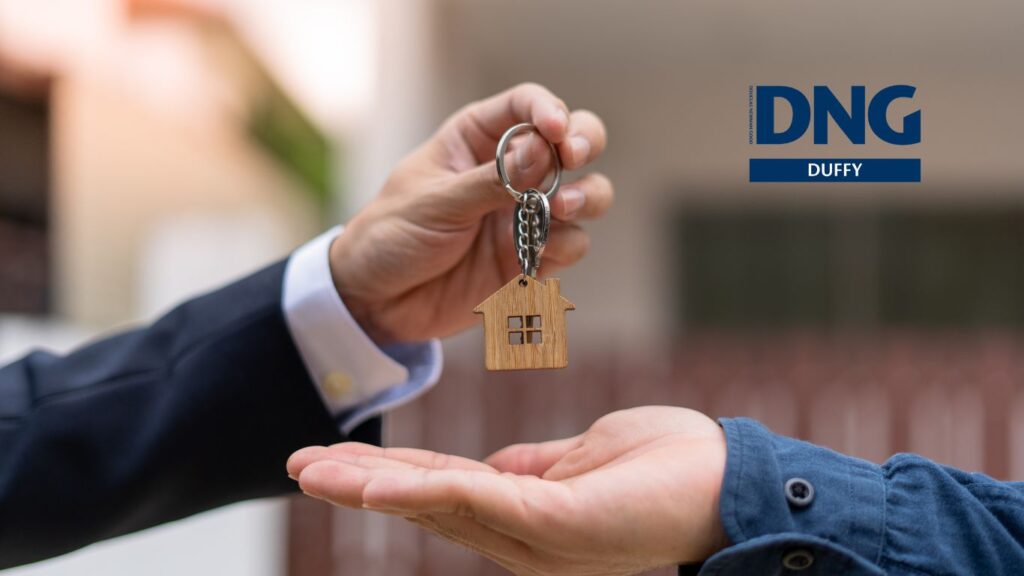 hands passing a model house keychain to a customer from an agent